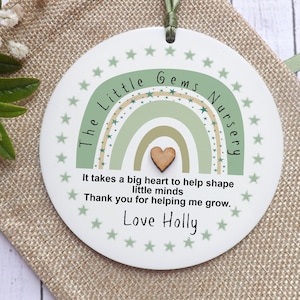 May include: A white round plaque with a green and beige rainbow design and the text "The Little Gems Nursery" and "It takes a big heart to help shape little minds. Thank you for helping me grow. Love Holly".