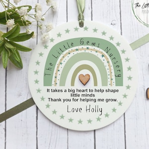 May include: A white round plaque with a green and beige rainbow design and the text "The Little Gems Nursery". The plaque also has the text "It takes a big heart to help shape little minds. Thank you for helping me grow. Love Holly".