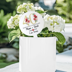 May include: A white round plant marker with gold glitter and red flowers. The marker says "Happy Ruby Anniversary Mum & Dad 1984 ♥ 2024 Love Daisy".