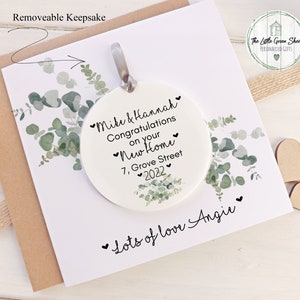 Pu&ograve; includere: Ciondolo in ceramica bianca con un design di eucalipto verde. Il ciondolo &egrave; personalizzato con il testo "Mike & Hannah Congratulazioni per la vostra nuova casa 7, Grove Street 2022" e "Tanto amore Angie".