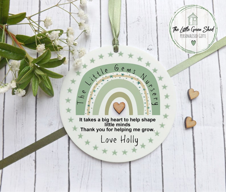 May include: A white round plaque with a green and beige rainbow design and the text "The Little Gems Nursery". The plaque also has the text "It takes a big heart to help shape little minds. Thank you for helping me grow. Love Holly".
