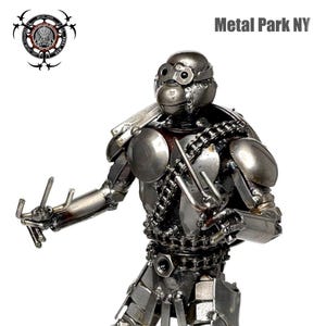 May include: A handcrafted metal sculpture of a figure, possibly a gorilla, with goggles and a chain belt. The sculpture is made of various metal pieces and has the text "Metal Park NY".