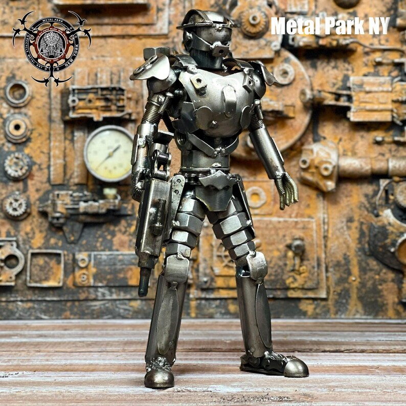 May include: A handcrafted metal sculpture of a futuristic soldier. The figure is made from various metal pieces, including nuts, bolts, and plates, and is holding a weapon. The background features industrial elements, and the text "Metal Park NY" is visible.