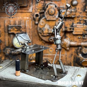 May include: A handcrafted metal sculpture depicting a figure at a desk, with a computer monitor and a golf club. The sculpture is made of various metal parts and has a steampunk aesthetic. The sculpture is on a wooden surface. The text "Metal Park NY" is visible.