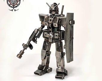 May include: A handcrafted metal robot sculpture, with a gun and shield. The robot is made of various metal pieces welded together, with a silver finish. The sculpture is standing on a white surface. The text "Metal Park NY" is at the bottom.