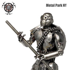 May include: A handcrafted metal sculpture of a turtle-like figure, holding a threaded rod. The sculpture is made from various metal pieces, including a chain around the shoulder. The text "Metal Park NY" is visible.