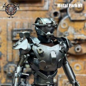 May include: A handcrafted metal sculpture of a humanoid figure, constructed from various metal pieces. The figure has a helmet, chest armor, and articulated arms. The text "Metal Park NY" is visible. The sculpture is set against a textured background.