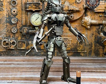 May include: A handcrafted metal sculpture of a Predator figure, standing on a wooden surface. The sculpture is made from various metal pieces, with intricate details. The figure is holding a weapon and has long, sharp claws. A standard D-cell battery is next to the figure. The text "Metal Park NY" is visible.