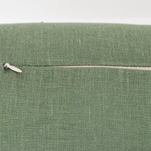 May include: A green linen cushion with a zipper closure. The zipper is visible and has a silver pull.