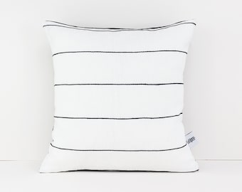 Könnte beinhalten: Ein weißes Kissen mit schwarzen horizontalen Streifen. Das Kissen hat ein kleines Etikett unten rechts, auf dem "Lauren Stripes" steht.
