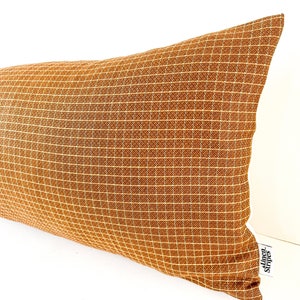 May include: A long, rectangular brown pillow with a subtle grid pattern. The pillow has a white border and a white tag that says "Linen Stripes".