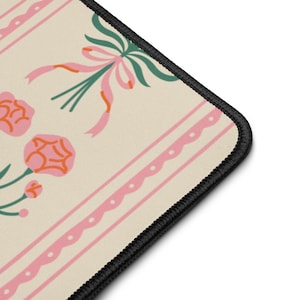 May include: A decorative mouse mat featuring a cream background with a floral design. The pattern includes pink roses, ribbons, and green leaves, with pink stripes and a black border.