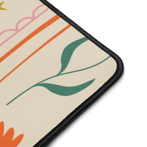 Könnte beinhalten: Ein cremefarbenes Mauspad mit einem schwarz genähten Rand. Das Design zeigt orange und rosa Streifen, grüne Blätter und eine orangefarbene Blume. Das Gesamtthema ist ein florales und abstraktes Design.