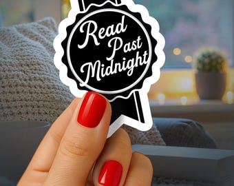May include: A black and white sticker with the text "Read Past Midnight" in a circular design. The sticker is held by a hand with red nail polish. The background is blurred, showing a window and a cozy interior.