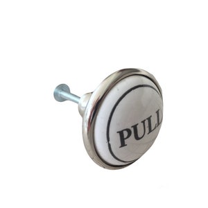 May include: White ceramic door knob with a silver metal base. The knob has the word "PULL" printed in black lettering.