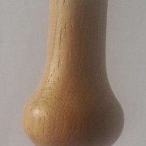 May include: A wooden bottle stopper with a pear-shaped design. The stopper is made of light brown wood with a natural grain pattern.