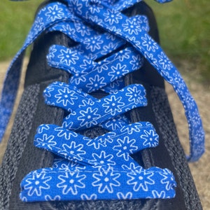 May include: Close-up of a black athletic shoe with bright blue shoelaces. The laces are patterned with white floral designs. The laces are tied in a bow at the top of the shoe.