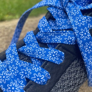 May include: Close-up of a black athletic shoe with bright blue shoelaces. The laces are patterned with white floral designs. The shoe's upper is a dark gray knit material.
