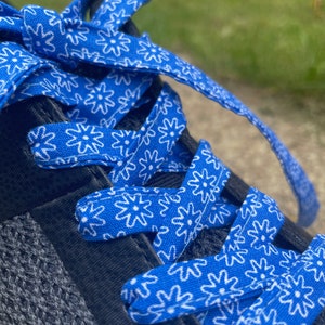 May include: Close-up of a blue and white floral patterned shoelace tied in a bow. The shoelace is threaded through a dark gray and black athletic shoe. The background is blurred.