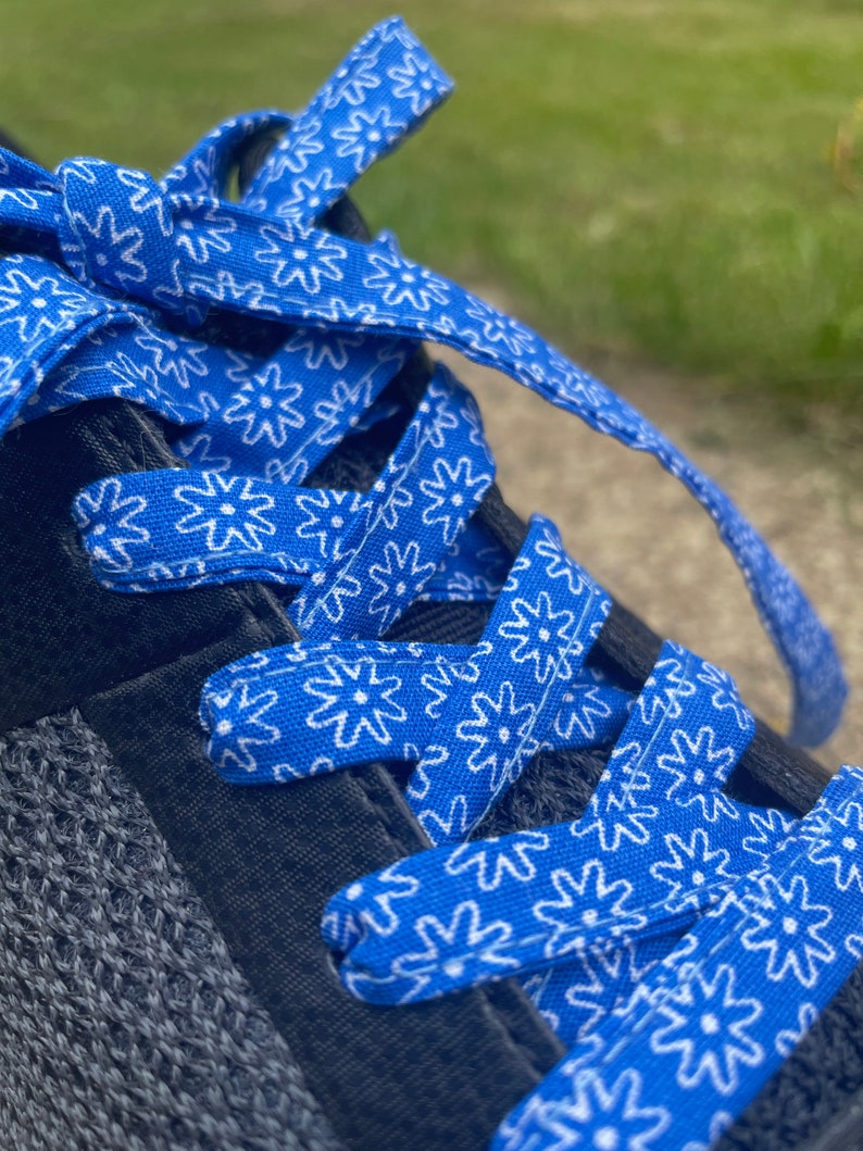 May include: Close-up of a blue and white floral patterned shoelace tied in a bow. The shoelace is threaded through a dark gray and black athletic shoe. The background is blurred.