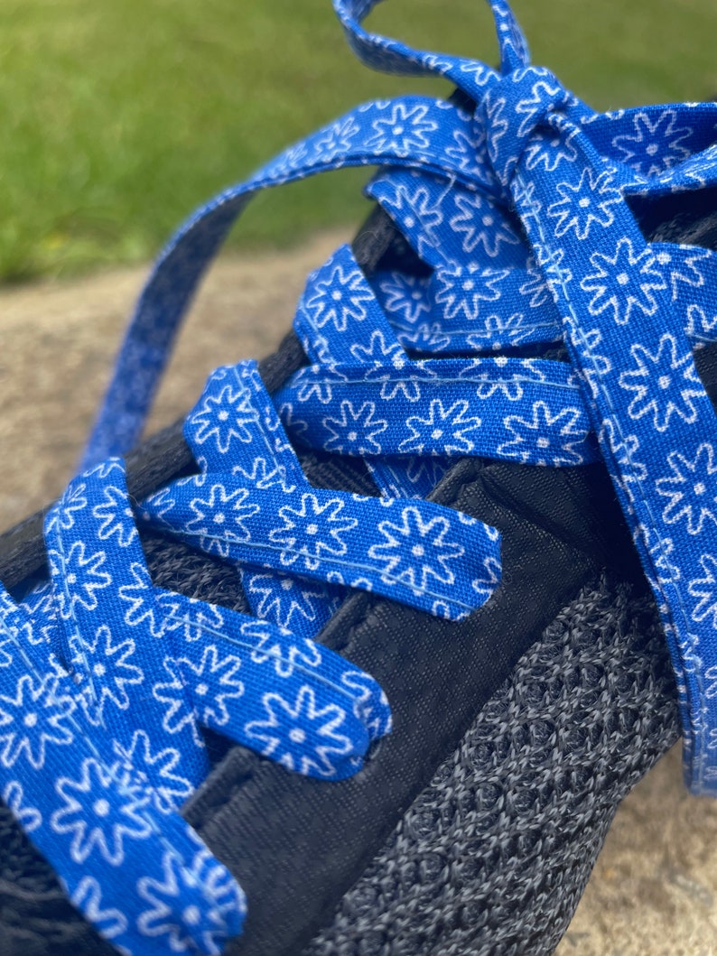 May include: Close-up of a black athletic shoe with bright blue shoelaces. The laces are patterned with white floral designs. The shoe's upper is a dark gray knit material.