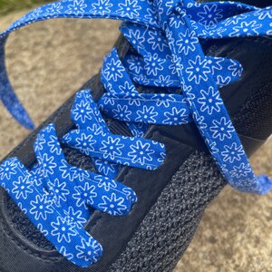 May include: Close-up of a black athletic shoe with bright blue shoelaces. The laces are patterned with white floral designs. The shoe's upper is made of a dark gray, breathable material.