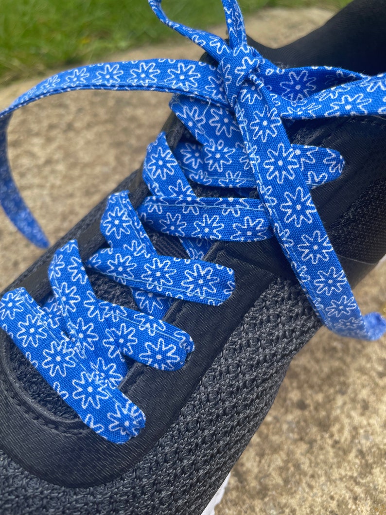 May include: Close-up of a black athletic shoe with bright blue shoelaces. The laces are patterned with white floral designs. The shoe's upper is made of a dark gray, breathable material.