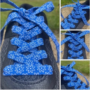 May include: Close-up of a black athletic shoe with bright blue shoelaces. The shoelaces are patterned with white floral designs. The laces are tied in a crisscross pattern.