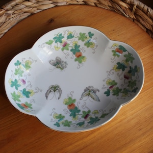 May include: A white porcelain scalloped dish featuring a delicate botanical pattern of green leaves, small yellow and purple flowers, and three detailed butterfly illustrations in shades of grey and green with a thin gold rim.