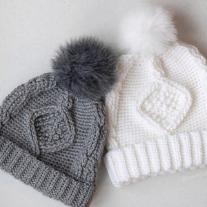 May include: Two knitted hats with pom poms. One hat is gray with a gray pom pom and the other is white with a white pom pom.