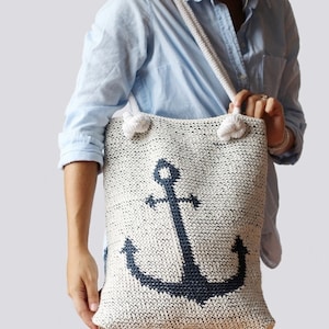 May include: A white crocheted tote bag with a blue anchor design. The bag has white rope handles.