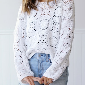 May include: White crochet sweater with a square pattern. The sweater has long sleeves and a loose fit.
