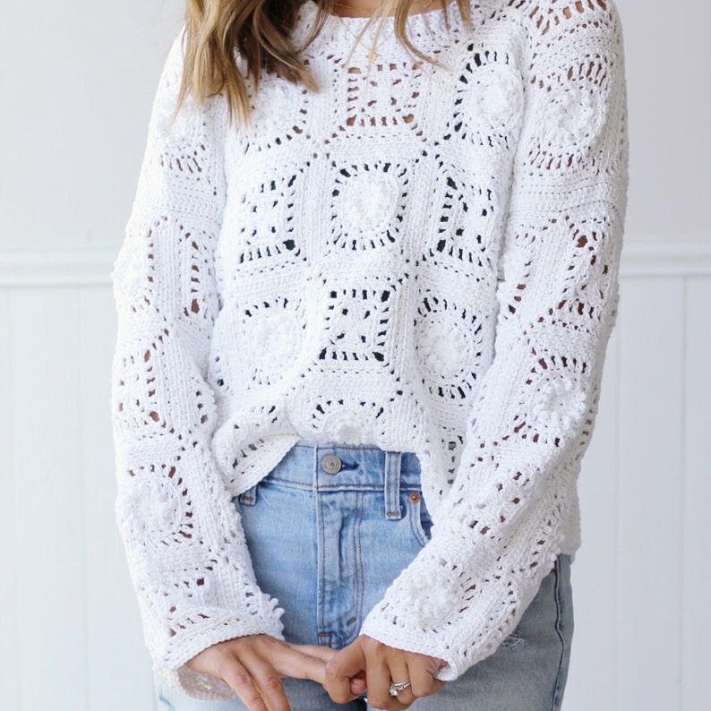 May include: White crochet sweater with a square pattern. The sweater has long sleeves and a loose fit.