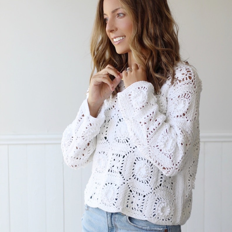 May include: A white crochet sweater with a loose fit and long sleeves. The sweater is made of a delicate, open-stitch pattern.