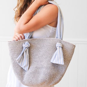 May include: A beige crocheted tote bag with blue and white striped fabric handles tied in bows.