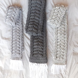 May include: Three crocheted scarves with white fringe. The scarves are in shades of gray, light gray, and dark gray.