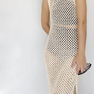 May include: A cream-colored crochet maxi dress with a loose fit and a side slit. The dress is made of a lightweight, breathable fabric and has a delicate, open-weave design.