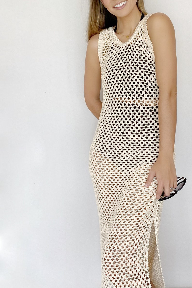 May include: A cream-colored crochet maxi dress with a loose fit and a side slit. The dress is made of a lightweight, breathable fabric and has a delicate, open-weave design.