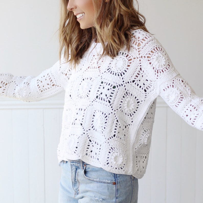 May include: White crochet sweater with a lacy, open-stitch design. The sweater has a relaxed fit and long sleeves.