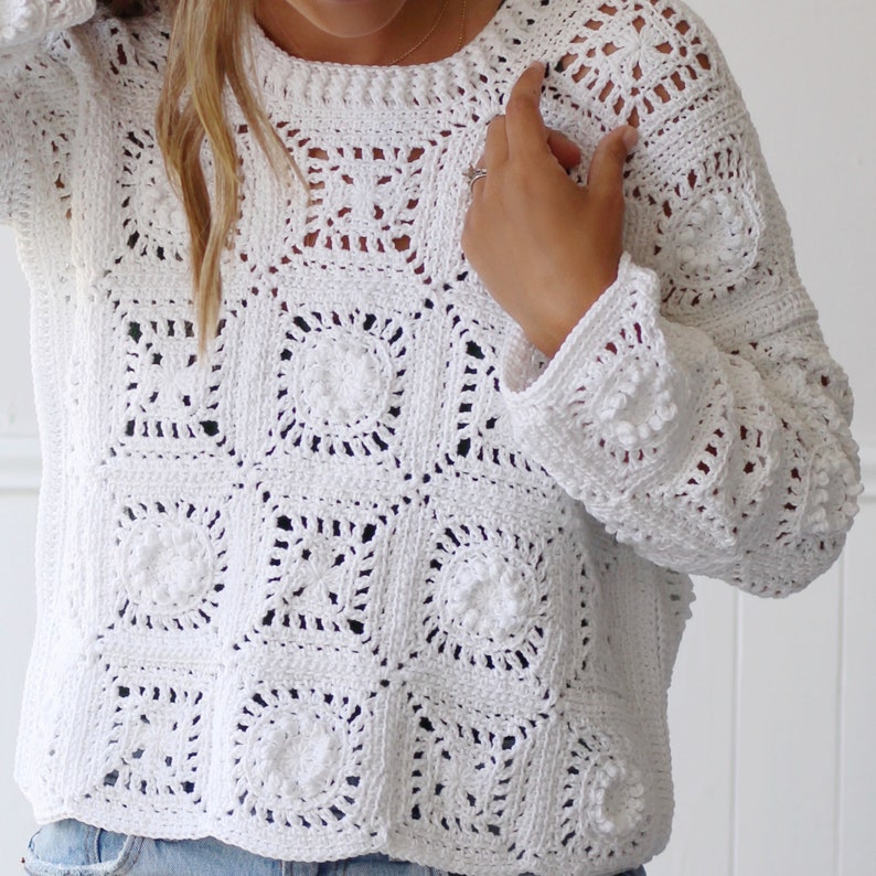 May include: White crochet sweater with a square pattern. The sweater has long sleeves and a loose fit.
