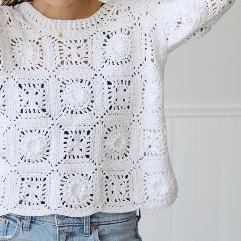 May include: White crochet sweater with a square pattern. The sweater has a round neckline and long sleeves.