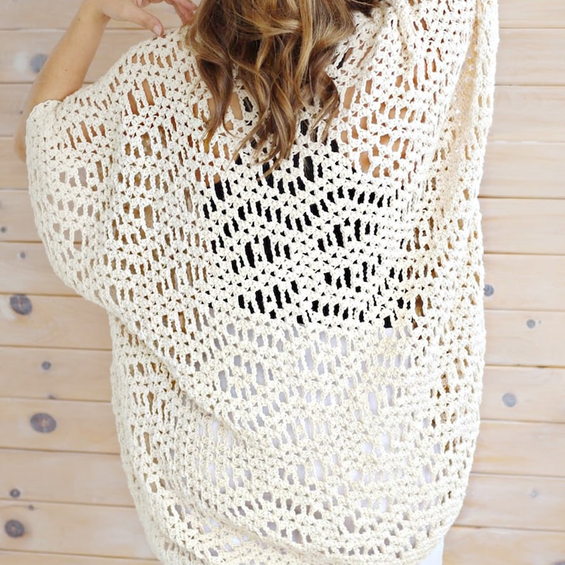 May include: A crocheted cardigan with a lacy openwork design in a cream color. The cardigan is lightweight and has a relaxed fit.