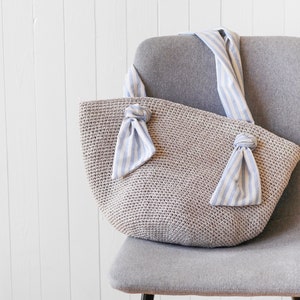 May include: A beige crocheted tote bag with blue and white striped fabric handles tied in bows.