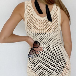 May include: A white crochet tank top with a black ribbon tied around the neck. The tank top is a loose fit and has a delicate, open-weave design.
