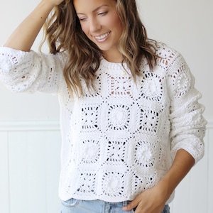 May include: White crochet sweater with a square pattern. The sweater has a relaxed fit and long sleeves.