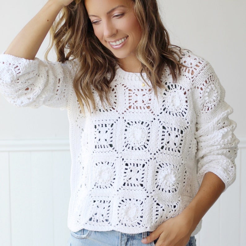 May include: White crochet sweater with a square pattern. The sweater has a relaxed fit and long sleeves.