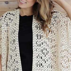 May include: A crocheted cream-colored cardigan with a loose fit and short sleeves. The cardigan is made with an open stitch pattern, creating a lightweight and airy feel.