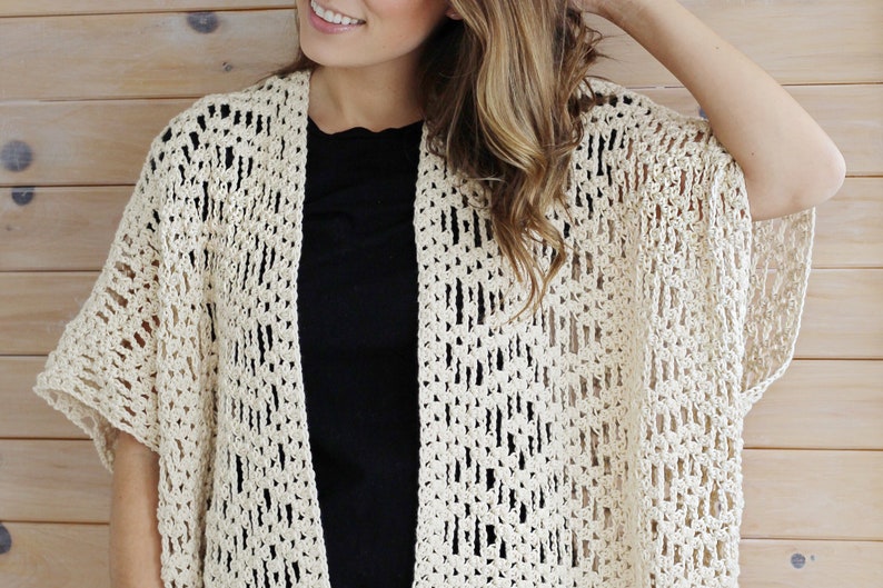 May include: A crocheted cream-colored cardigan with a loose fit and short sleeves. The cardigan is made with an open stitch pattern, creating a lightweight and airy feel.