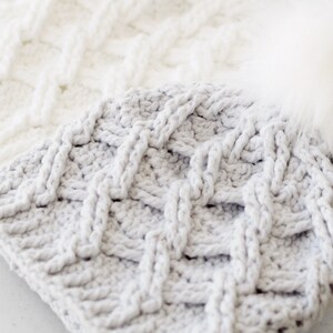 May include: Two crocheted hats, one white and one gray, with a braided pattern. The gray hat has a white faux fur pom pom.