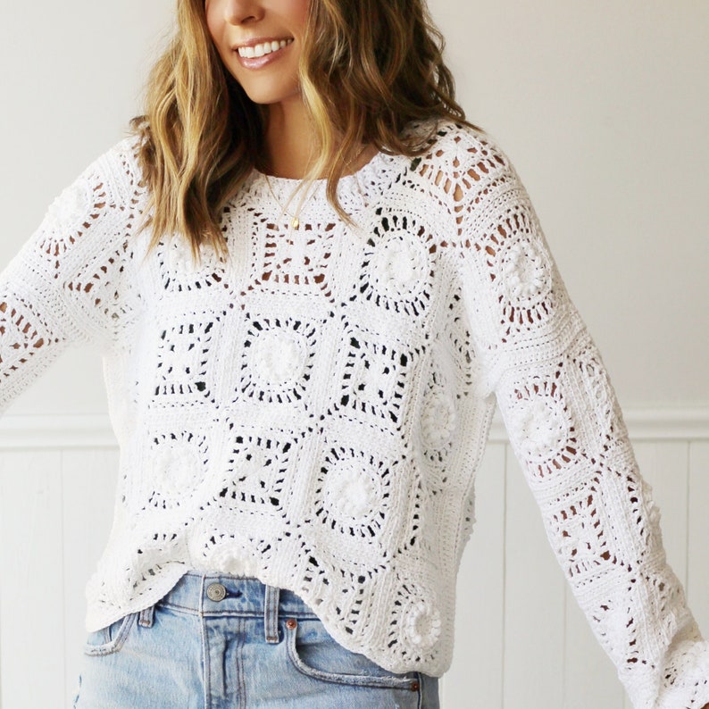 May include: White crochet sweater with a square pattern and long sleeves. The sweater is made of a lightweight, airy fabric and has a relaxed fit.